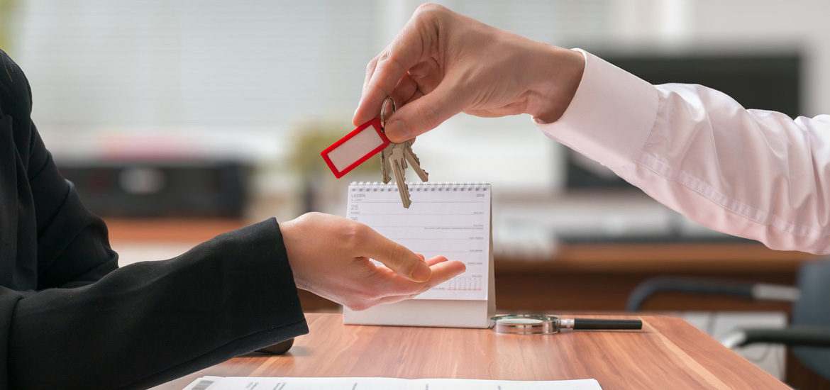 Real estate concept. Realtor is passing keys to the client sitting behind desk with contract